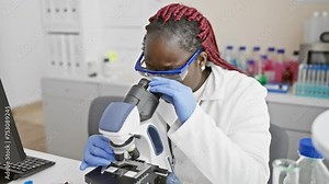African woman scientist using microscope in laboratory setting, portraying research and healthcare concept